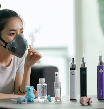 A concerned young mother holding a protective mask while examining vaping devices on a table, reflecting on indoor air quality and family health.